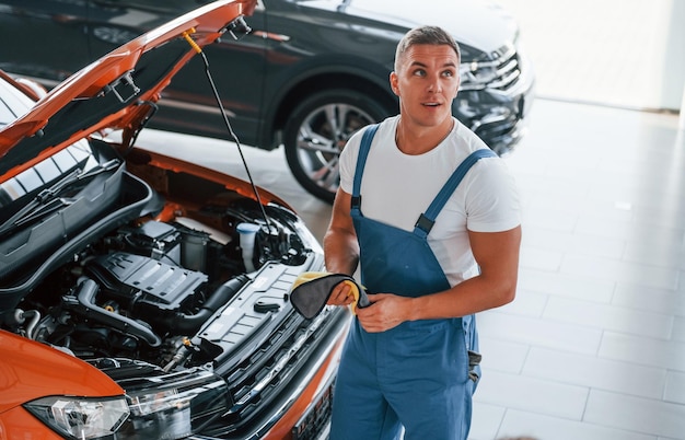 Foto oranje gekleurde auto man in uniform repareert kapotte auto binnenshuis