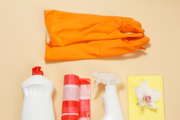 Oranje handschoenen, plastic flessen met vloeibare vuilniszakken en sponzen op een beige achtergrond