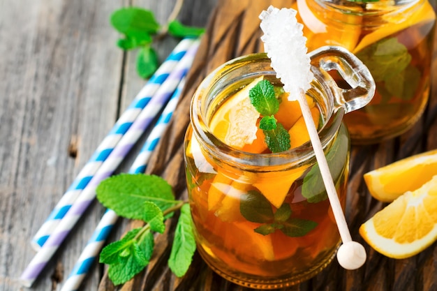 Oranje ijsthee met muntblaadjes in een glazen pot op het oude houten oppervlak