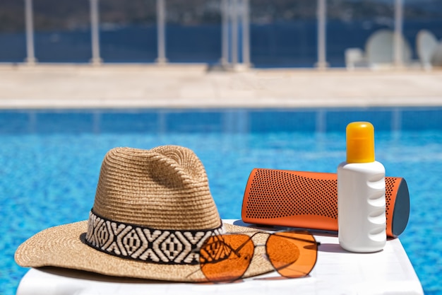 Oranje kleurige strandaccessoires bij zwembad. Zonnebrandcrème, zonnebril, muziekspeaker en strohoed.