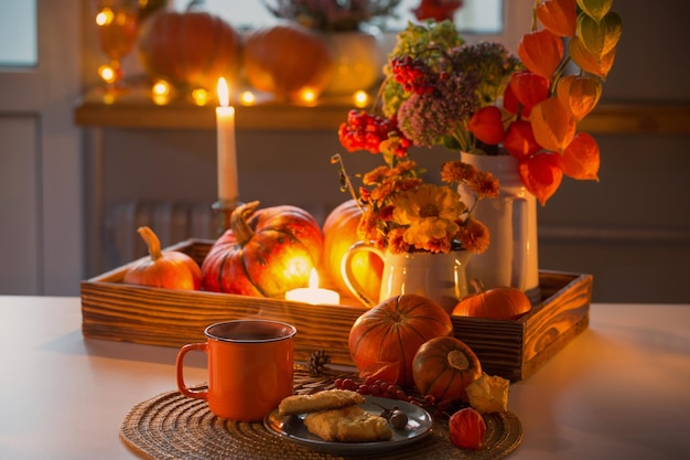 Oranje kopje thee en herfstdecor met pompoenbloemen en brandende kaarsen op tafel