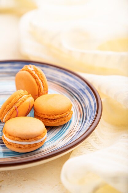 Oranje macarons of bitterkoekjes taarten met kopje koffie op een witte betonnen ondergrond en linnen textiel. Zijaanzicht, close-up, selectieve aandacht.