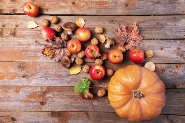 Oranje pompoen met cardoncellipaddestoelen, appels, walnoten en kleurrijke bladeren op oude rustieke houten planken.