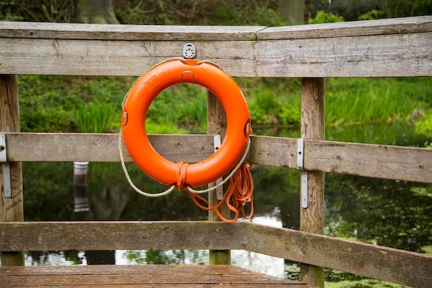 Oranje reddingsgordel die aan een houten reling bij de rivier hangt