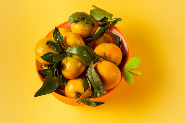 Oranje rijp Mandarijn fruit met groene bladeren in een kom, op gele achtergrond.