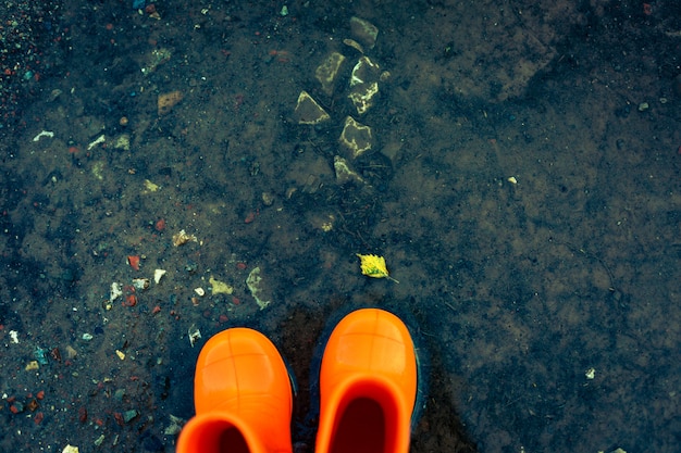 Oranje rubberlaarzen die zich in een vulklei met gevallen blad bevinden