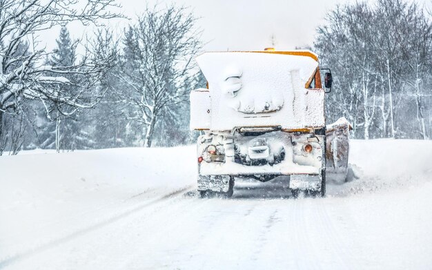 Oranje snelweg onderhoud strooiwagen ploegwagen volledig bedekt met sneeuw, bosweg schoonmaken, uitzicht vanaf auto die erachter rijdt.