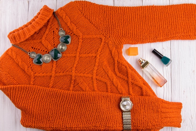 Oranje trui met accessoires en cosmetica. Vrouwelijke outfit op houten achtergrond