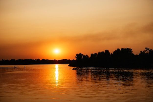 Oranje zonsondergang op de rivier met boomsilhouetten