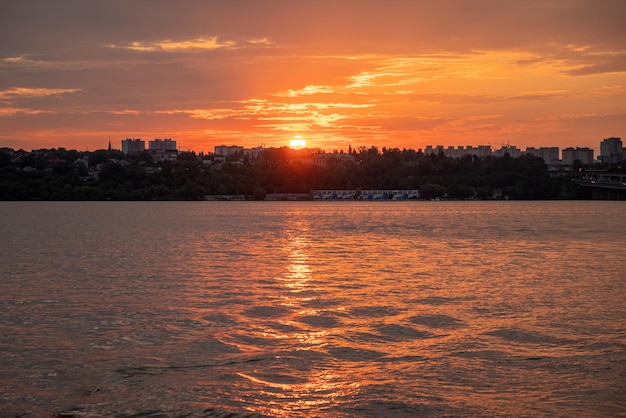 Oranje zonsondergang over de rivier, stadsgebouwen afgetekend aan de horizon