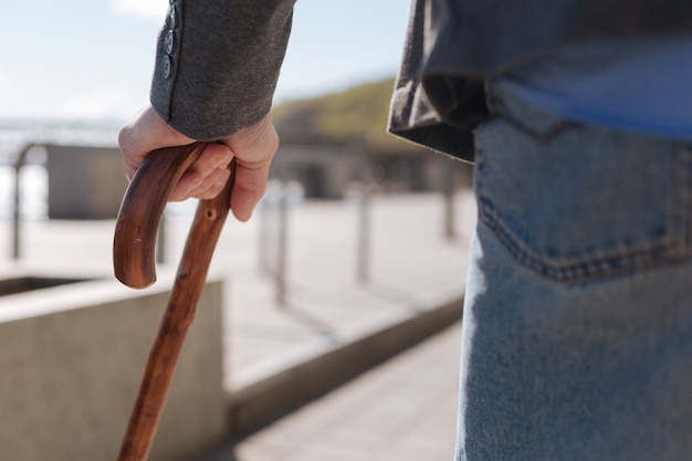 写真 普通の穏やかな年配の男性が歩きながら特別な道具を使って足に問題を抱えている