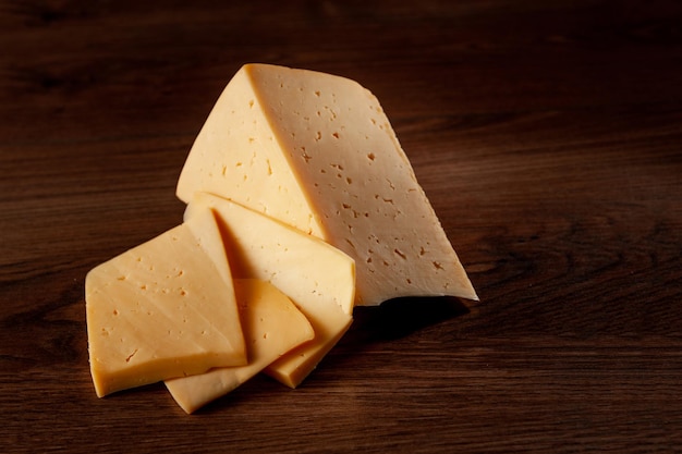 Обыкновенный сыр на деревянном фоне, нарезанный ломтиками, лежит на столе