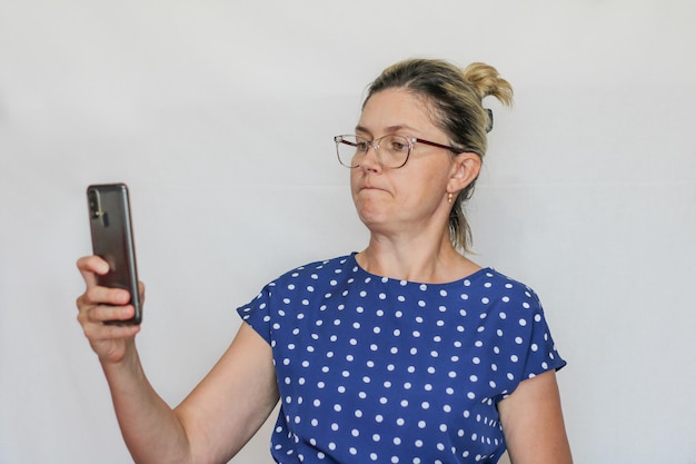 An ordinary middleaged woman on a white background looks at the\
phone