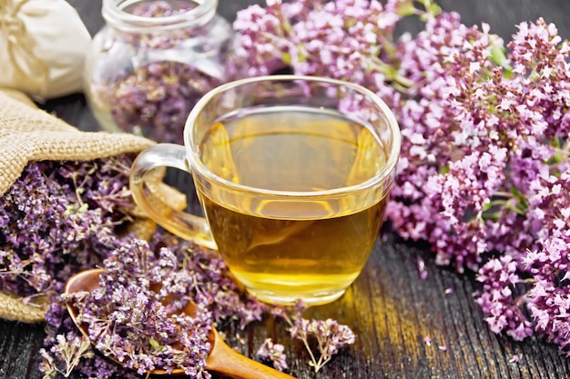 Oregano herbal tea in a glass cup, fresh flowers, dried marjoram flowers in a bag, jar and spoon