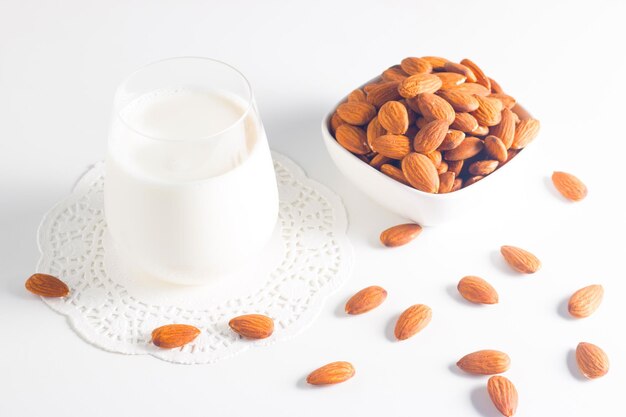 Organic almond milk in glass with raw almonds on white table