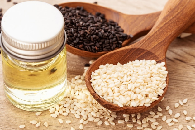 Organic Black and white sesame seeds in wooden spoon with oil bottle