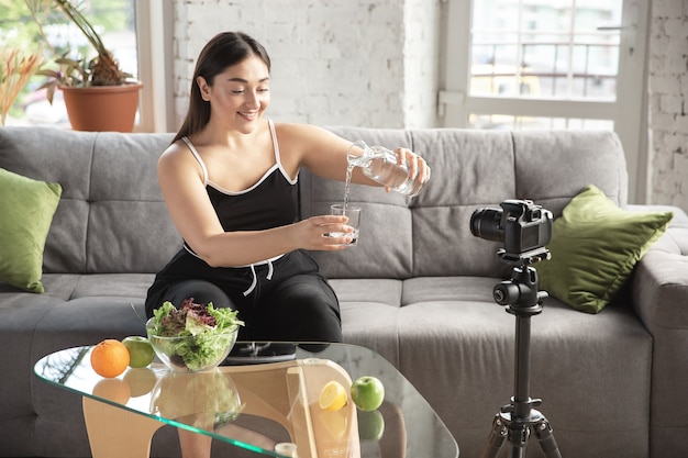 사진 본질적인. 백인 블로거, 여성은 다이어트와 체중 감량 방법을 vlog로 만들고 몸에 긍정적이고 건강한 식생활을 합니다. 카메라를 사용하여 그녀의 과일 샐러드 준비를 녹화합니다. 라이프 스타일 인플루언서, 웰빙 개념.
