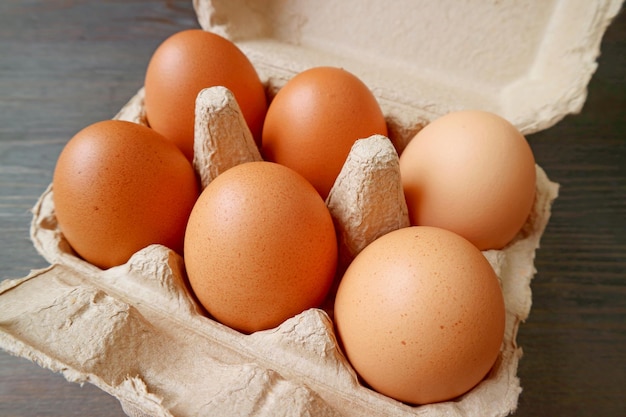 Uova di gallina organiche in scatola di cartone di carta su fondo di legno nero