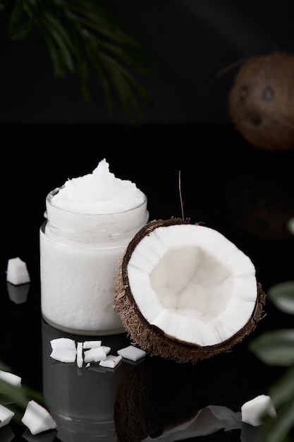 Organic coconut oil and half coconut, close-up on a dark mirrored table. Selective focus on a nut, vertical frame. Organic Spa Oil, Skin and Body Health Care