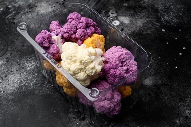 Organic colorful cauliflowers in container on black dark stone table background