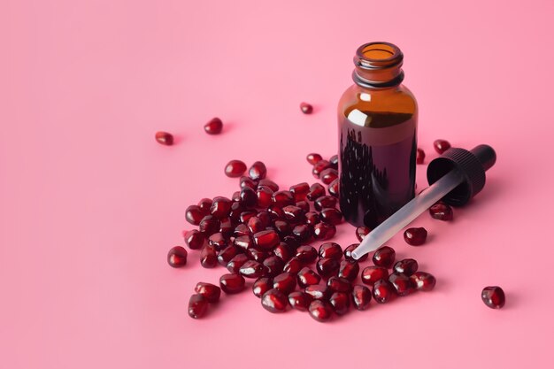 Organic cosmetic pomegranate seed oil in brown dropper bottle on pink surface.