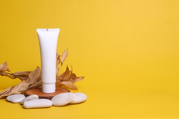 Organic cosmetic product mock up white tube on wooden pedestal decorated with dried leaves and whit