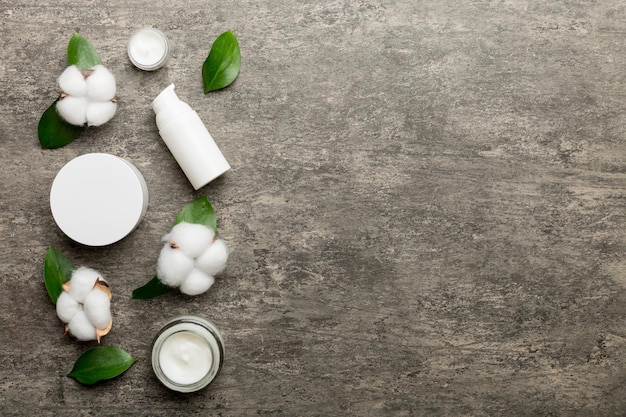 Organic cosmetic products with cotton flower and green leaves on cement background. Copy space, flat lay.