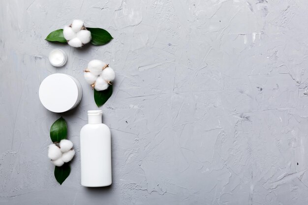 Organic cosmetic products with cotton flower and green leaves on cement background. Copy space, flat lay.