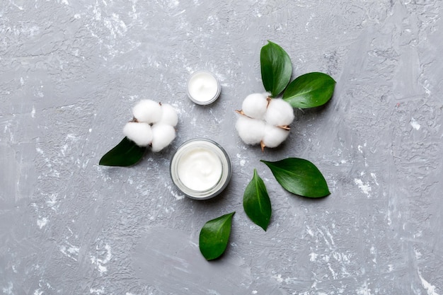 Organic cosmetic products with cotton flower and green leaves on cement background Flat lay