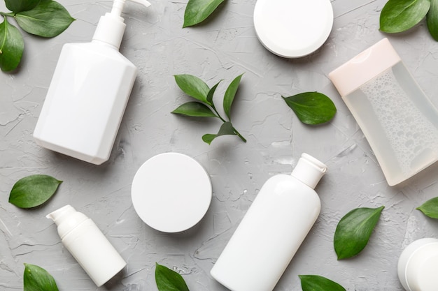 Organic cosmetic products with green leaves on cement background. Flat lay.