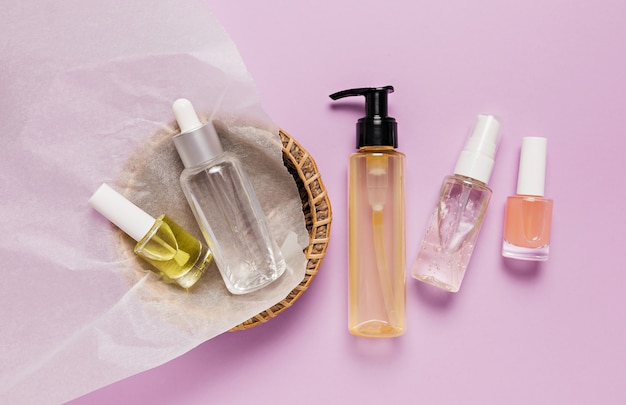 Organic cosmetics packaging design. Flat lay, top view clear glass pump bottle, brush jar, moisturizing serum jar in a paper basket on a purple background. Natural cosmetics SPA