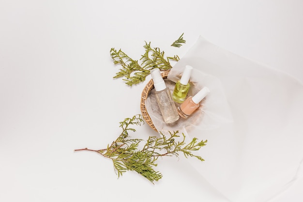 Organic cosmetics with plant. Flat lay, top view clear glass pump bottle, brush jar, moisturizing serum jar in a paper basket on a white background. Natural cosmetics SPA