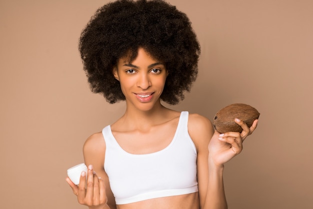 Organic cosmetics. A young pretty curly-haired mulatta with a coconut and a jar of cream