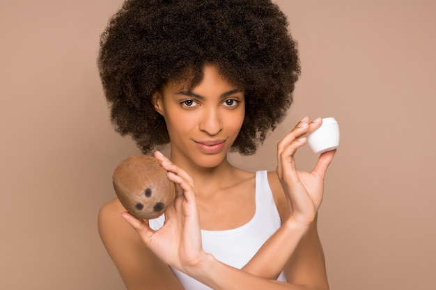 Organic cosmetics. A young pretty curly-haired mulatta with a coconut and a jar of cream