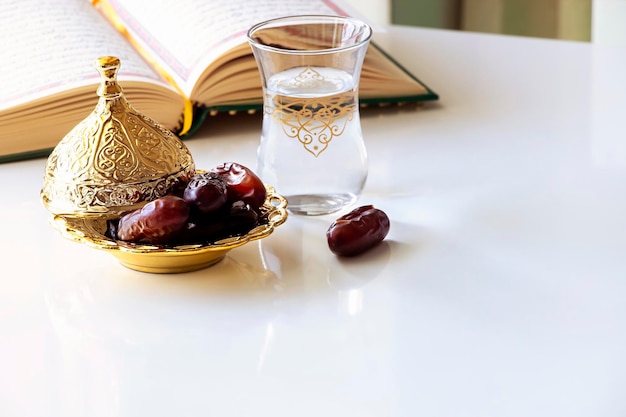 Foto date organiche in piatto d'oro tazza d'acqua e libro del quran iftar ramadan concept copia spazio