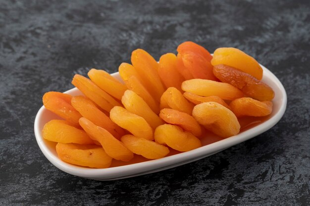 Organic dried apricots on plate on dark background