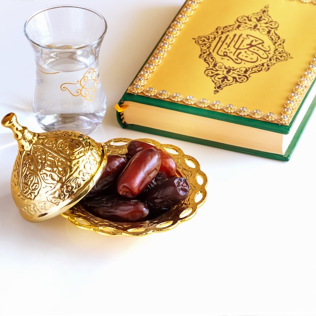 Organic dried dates arabic golden plate, cup water and quran book.