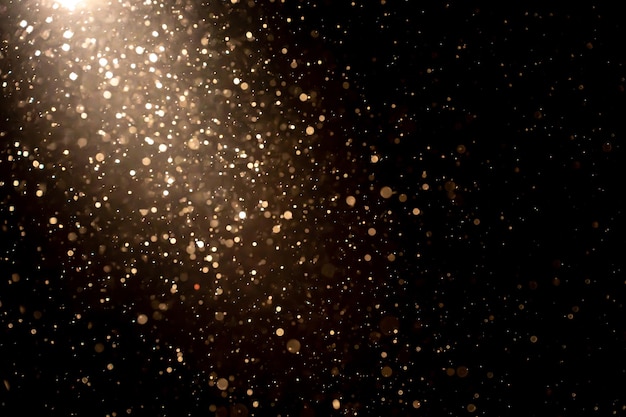 Organic dust particles floating in light ray on black background. Glittering sparkling glowing.