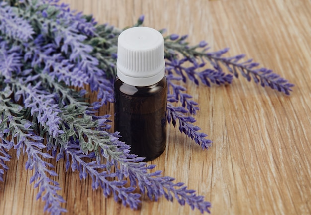 Organic essential oil in bottle and lavender flowers on wooden