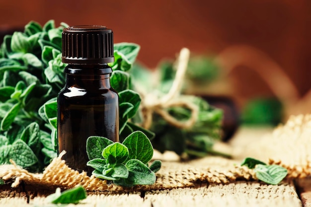 Organic essential oregano oil in a glass jar and a bunch of fresh marjoram vintage wooden background selective focus