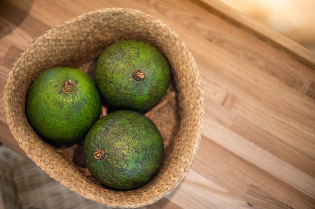 Organic farm avocado in straw basket on wooden table closeup\
fresh ripe green exotic fruits