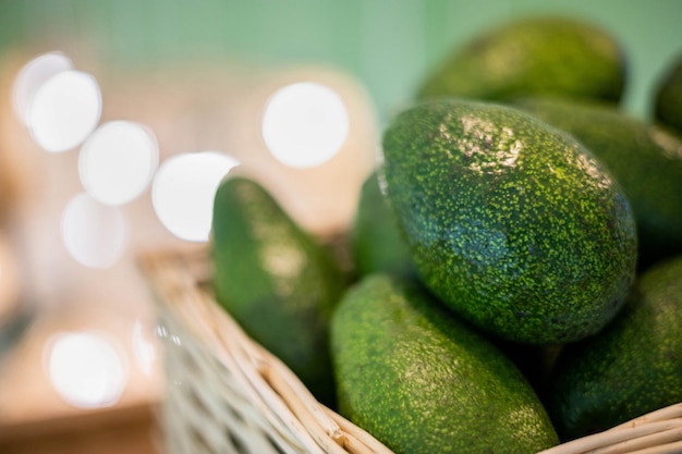 Avocado biologico in cesto di paglia su tavola di legno primo piano frutti esotici verdi maturi freschi