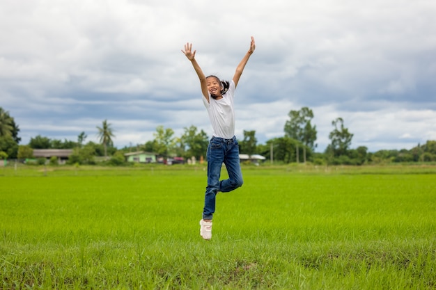 In an organic farmed rice field, happy Asian children jumping raise their hands to the sky and grin.