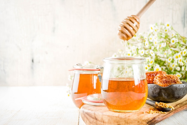 Organic floral honey, in jars, with pollen and honey combs, on a white wooden table, with wildflowers