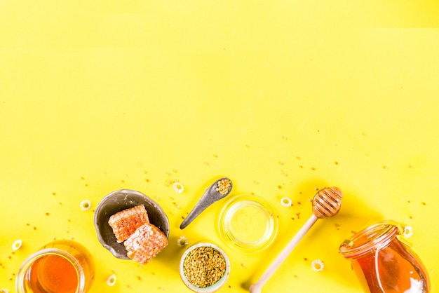 Organic floral honey, in jars, with pollen and honey combs, with wildflowers creative layout bright yellow background top view copy space