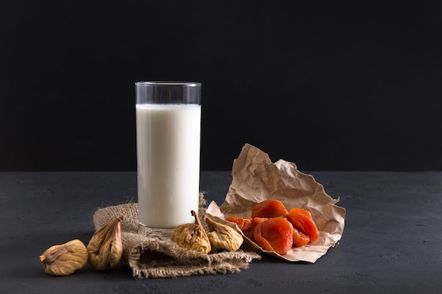 Organic food. Glass of milk or yoghurt with nuts and dried apricot, still life on black background