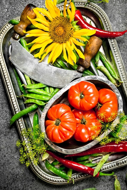 Foto cibo organico. piselli, pomodori e peperoncino piccante su un vassoio in acciaio. su una superficie rustica.