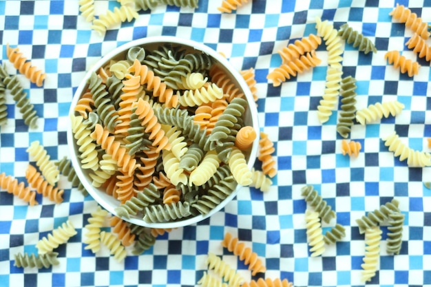 Organic fusilli tricolore spilling on pink background