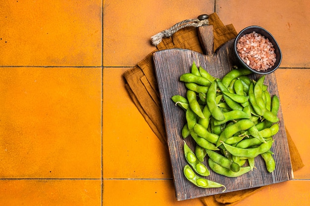 Organic green edamame beans raw soy beans on wooden board orange background top view copy space