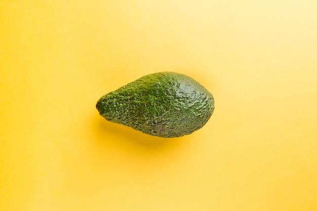 Organic green whole avocado fruit on yellow background. Top view. Pop art design, flat lay style